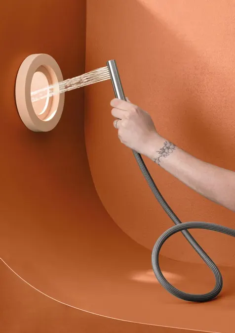 A hand holding a Fontea brushed steel shower wand against an orange wall